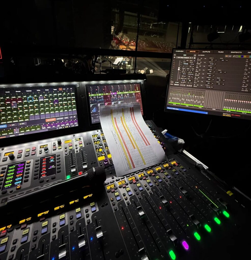 Console de mixage numérique professionnelle en régie retour (Monitor) lors d'un concert live avec écrans tactiles et faders éclairés.