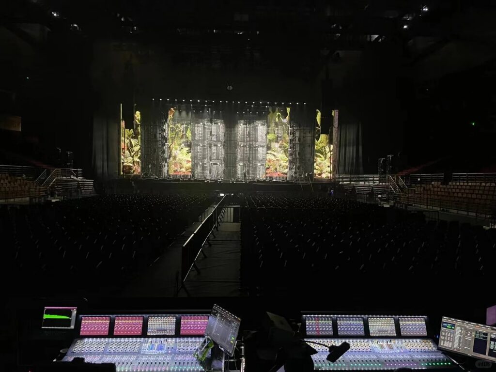 Régie technique FOH (Front of House) avec consoles de mixage numériques grand format face à une scène de concert monumentale équipée d'écrans LED.